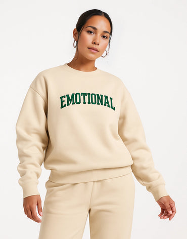 Person wearing a beige sweatshirt with 'EMOTIONAL' in green text on a white background