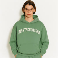 Person wearing a green hoodie with 'UNENTSCHLOSSEN' text on a white background