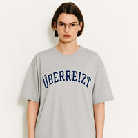 Person wearing a gray t-shirt with 'UBERREIZT' text on a white background